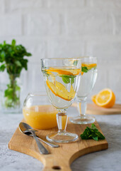 A drink made of water, lemon and honey in a transparent glass on a wooden stand. Light background, vertical orientation, side view.