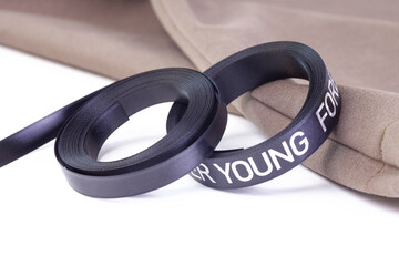 close-up of two coils of black satin ribbon on a stack of hoodies or T-shirts on a white background.