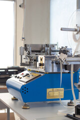 side view professional equipment on the table in the factory, blue Chinese cold or hot elastic tape cutting machine, satin ribbon cutter for labels or tags.