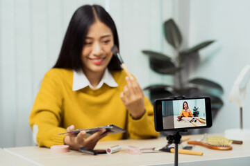 Asian teenage girls doing makeup vlogs and using a video mobile camera to record vlogs and publish them online at home.