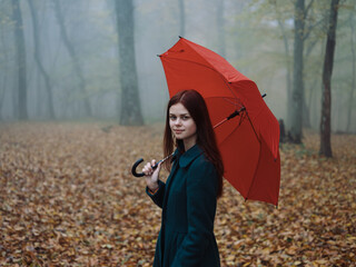 Pretty woman with red umbrella in autumn on nature yellow leaves walk