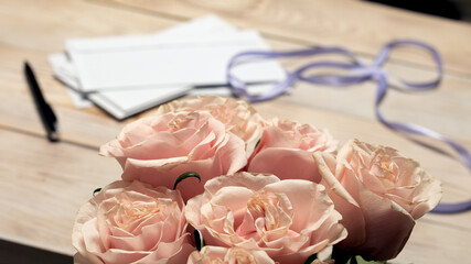 Flowers of bouquet of pink roses on blurry background from stack of papers on lighted table. preparing invitations, writing letters