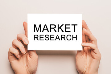 Female hands hold card paper with text Market Research on a yellow background. Business and finance concept