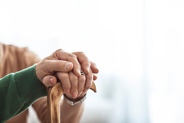 Cropped shot of senior couple holding hands while sitting together. Focus on hands on walking stick. Retirement couple holding hands. Cropped shot of a senior couple holding hands