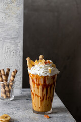 Milkshake glass with whipped cream and caramel decorated with candied fruit  and wafer rolls on dark background. Sweet delicious drink