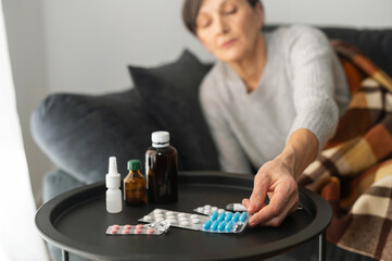 Tablets, pills and different treatment remedies on the table near couch, a senior woman in out of focus taking a one