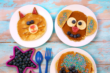Fun food for children. Cat and dog shaped pancakes on white plates, blue wooden background, top view. Creative idea for kids breakfast.	
