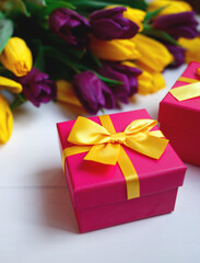 pink gift box with yellow bow on the background of a bouquet of tulips
