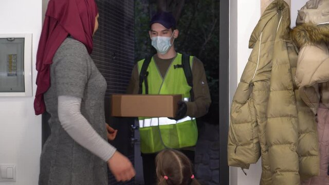 Delivery in the month of Ramadan. A volunteer wearing a medical mask and gloves delivers blessed zakat and sadaqa gifts to Muslim family in need. Humanitarian assistance