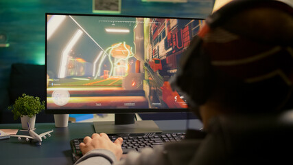 Back shot of pro esport gamer playing first person shooter game on powerful computer using RGB keyboard. Competitive player man streaming online video game for tournament using professional equipment