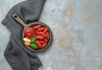 Smoked sausages with garlic and ketchup on a wooden plate with a handle on a gray background with a napkin.