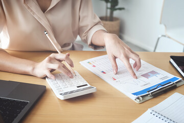 Business woman using calculator to review balance sheet annual  using  document and laptop computer...
