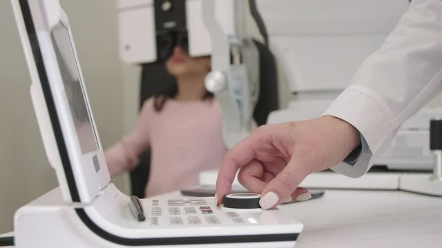Closeup of unrecognizable female doctor adjusting eye chart projector while little girl doing her eye vision exam in modern clinic