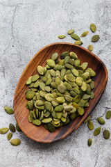 Wooden plate with pumpkin seeds on a gray concrete background