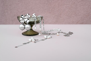 Glass goblet with stylish jewelry set of different earrings and chains on pastel surface. Creative...