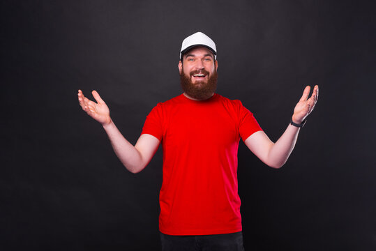 Photo of cheerful young bearded man in red t-shirt making welcome gesture