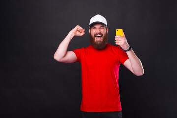 Fototapeta premium Photo of amazed young bearded man celebrating and holding smartphone