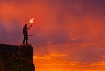 Concept of confidence - Man on a cliff with a torch and sword