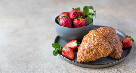 French crispy croissants with strawberry on a plate and berries in a bowl, concrete background. Freshly baked croissant. Idea for breakfast or dessert.