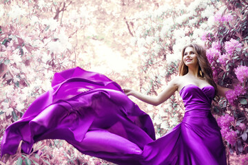 Fototapeta premium Fashion Woman Pink Dress in Spring Flower Garden. Beauty Model Girl in Purple Silk Gown Fluttering on Wind. Floral Pink Fantasy Background