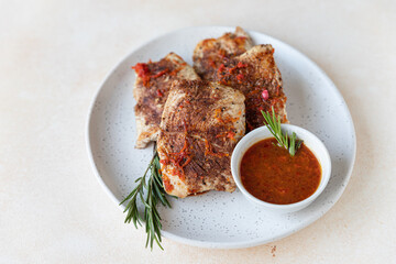 Fried turkey or chicken breast served with orange sauce and rosemary on a plate, light concrete background. Healthy food.
