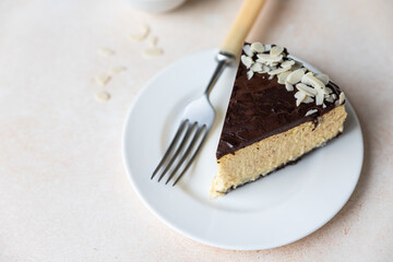 Slice of no baked creamy cheesecake with chocolate glaze and almond, light concrete background.