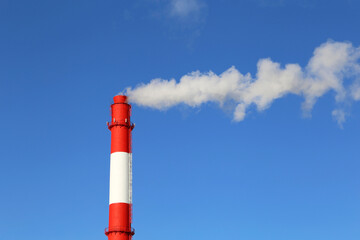 Factory chimney on blue sky background with white smoke. Concept of steam plant, air pollution, heating season