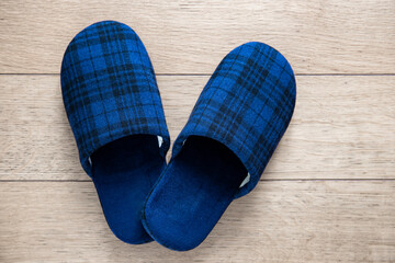 Blue slippers on parquet floor. Picture taken at home representing a pair of tartan fabric slippers abandoned on the floor.