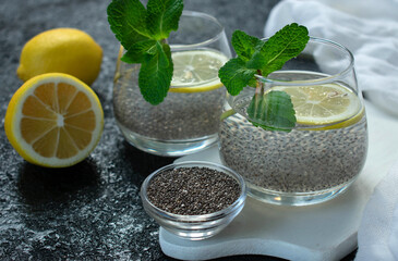 Two glasses of water with chia seeds and lemon on a black background.