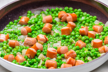 mixture of green peas with sausage in frying pan
