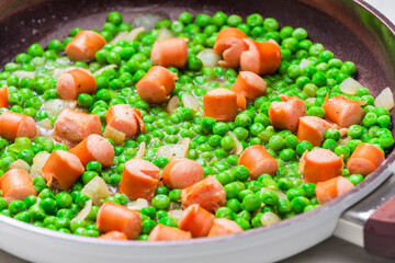 mixture of green peas with sausage in frying pan