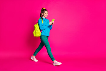 Fototapeta na wymiar Full length photo of pretty sweet woman dressed blue hoodie backpack chatting modern gadget isolated pink color background