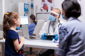 Pediatry specialist talking with little child about healtcare illness in medical clinic. Doctor in treatment disease wearing protective face mask against covid19 during global pandemic