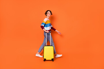 Full body profile portrait of charming person hand carry suitcase walking look camera isolated on orange color background