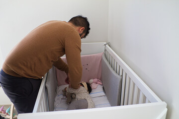 Obraz na płótnie Canvas homosexual couple have put their baby daughter to bed in her cot and they are covering her up with sheets.