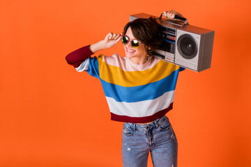 Photo of funny pretty young lady dressed striped pullover arm dark glasses holding boom box isolated orange color background