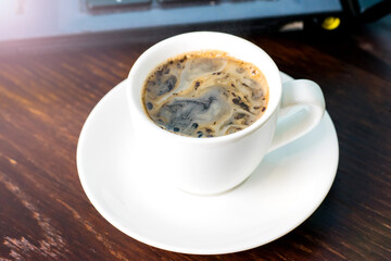 Coffee in a white cup and a laptop on the background on a brown wooden table. Concept of remote work or training, the start of the working day in the office.