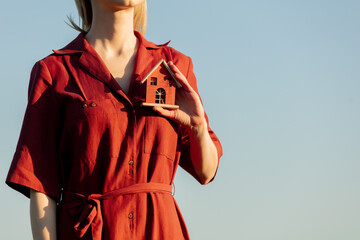 Woman in red dress hold little toy house on green wheat field in background