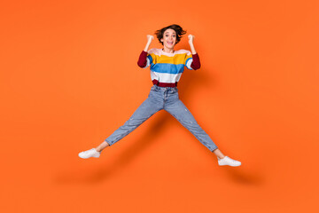 Fototapeta na wymiar Full size photo of astonished lady jumping high fists up celebrate triumph isolated on orange color background