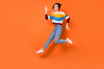 Fototapeta na wymiar Photo of funky adorable young lady dressed striped pullover jumping waving arm isolated orange color background