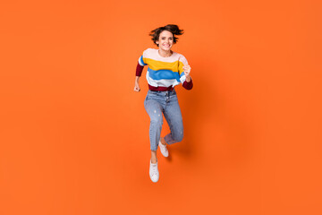 Fototapeta na wymiar Photo of pretty cute young woman wear striped sweater jumping running fast isolated orange color background