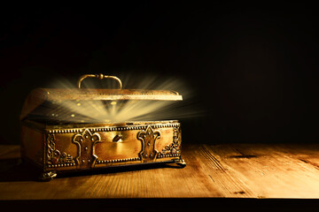Image of mysterious magical treasure chest with light over wooden old table and dark background