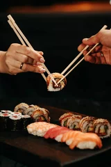 Foto op Canvas Man and woman pick up sushi with chopsticks at the same time © alexblackphoto
