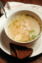 Close-up of chicken broth in a white plate with slices of bread
