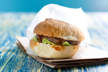 Burger with beef, sauce and salad in a craft bag for food on a bright blue background copy space. Food delivery concept, restaurants operating in quarantine covid 19