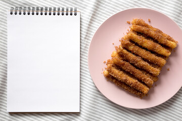 Home-baked Churro Bites on a pink plate, blank notepad, top view. Flat lay, overhead, from above.