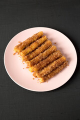Home-baked Churro Bites on a pink plate on a black surface, side view.