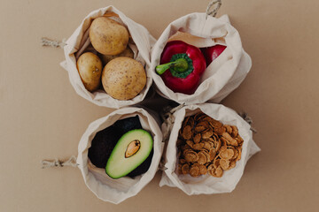 Reusable storage bags for vegetables and fruits on cardboard background. Storage bags with potatoes, avocado, red pepper, flakes. Healthy food in storage bags.