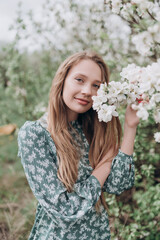 Fototapeta premium beautiful girl with brown hair in a green dress in a blooming apple orchard with white flowers