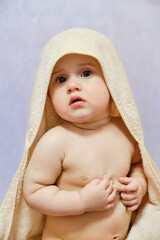 Baby girl after shower or bath with towel on head. Baby wearing hooded towel sitting on parents bed after bath or shower.